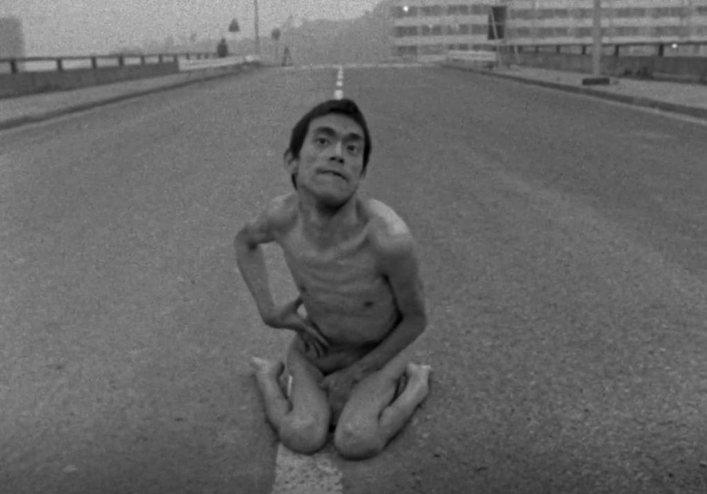 全身赤裸的橫田弘坐在馬路中央面對鏡頭，赤祼的告白，其後在地上拼命地掙扎前行，似是對命運不公的無聲吶喊，直接而震撼，充滿張力。（影片截圖∕香港藝術節允准）