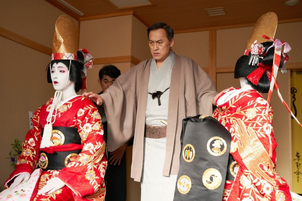 電影第一男主角喜久雄（吉澤亮飾演）與第二男主角俊介（橫濱流星飾演）一同演出《京鹿子娘道成寺》之際，登場前的後台一景。左為俊介，右為喜久雄。中間者為花井家家主花井半二郎（渡邊謙飾演）。（網上圖片）