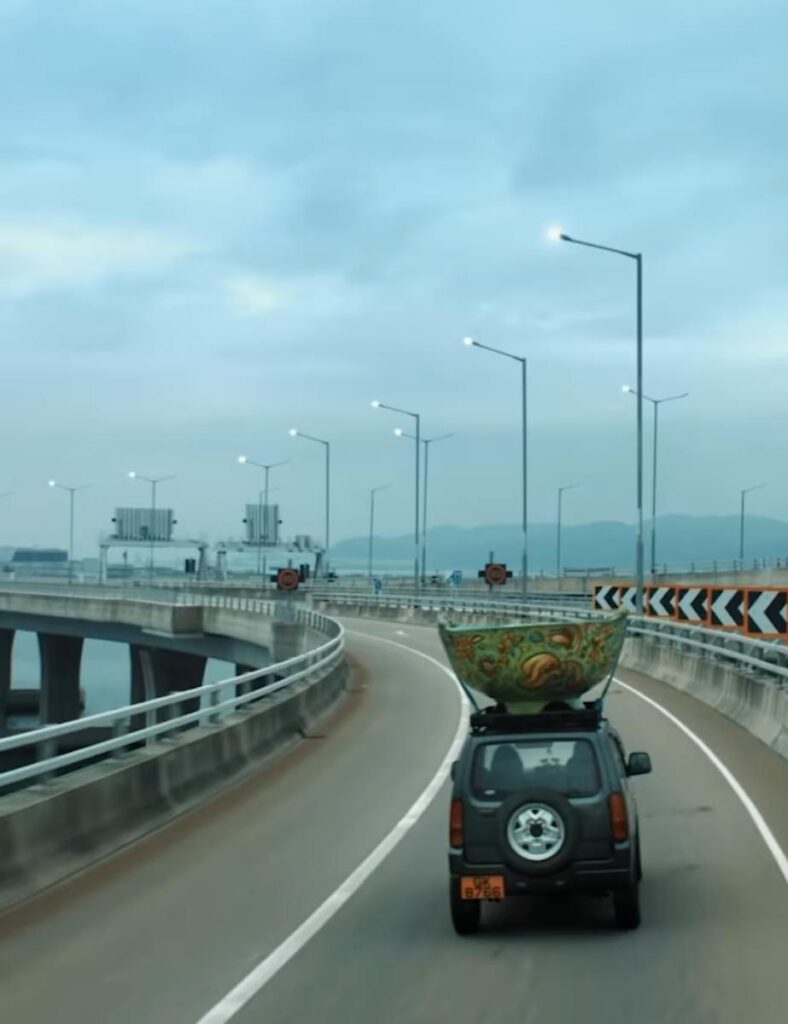 《我阿爹想旅行》中有不少公路上汽車飛馳的場面,車頂運載著巨型道具碗子,構成獨特的景觀(網上圖片)。